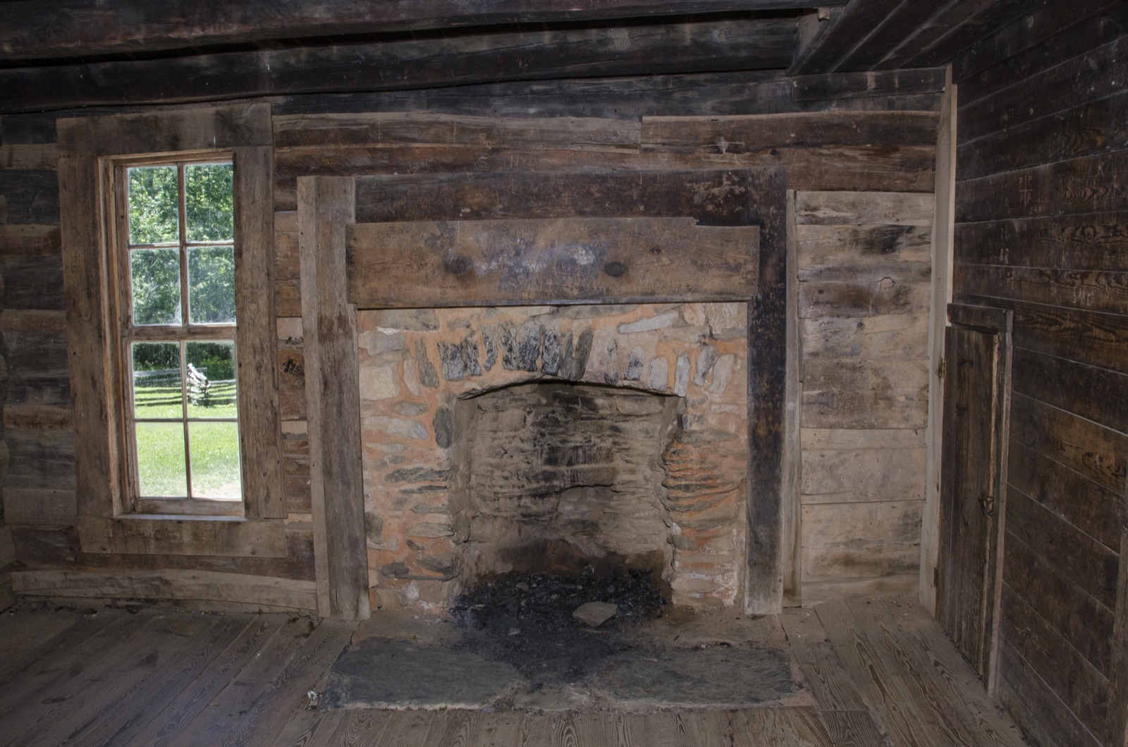 The log interior of the John Oliver cabin in Cades Cove, with a stone fireplace and a small window.