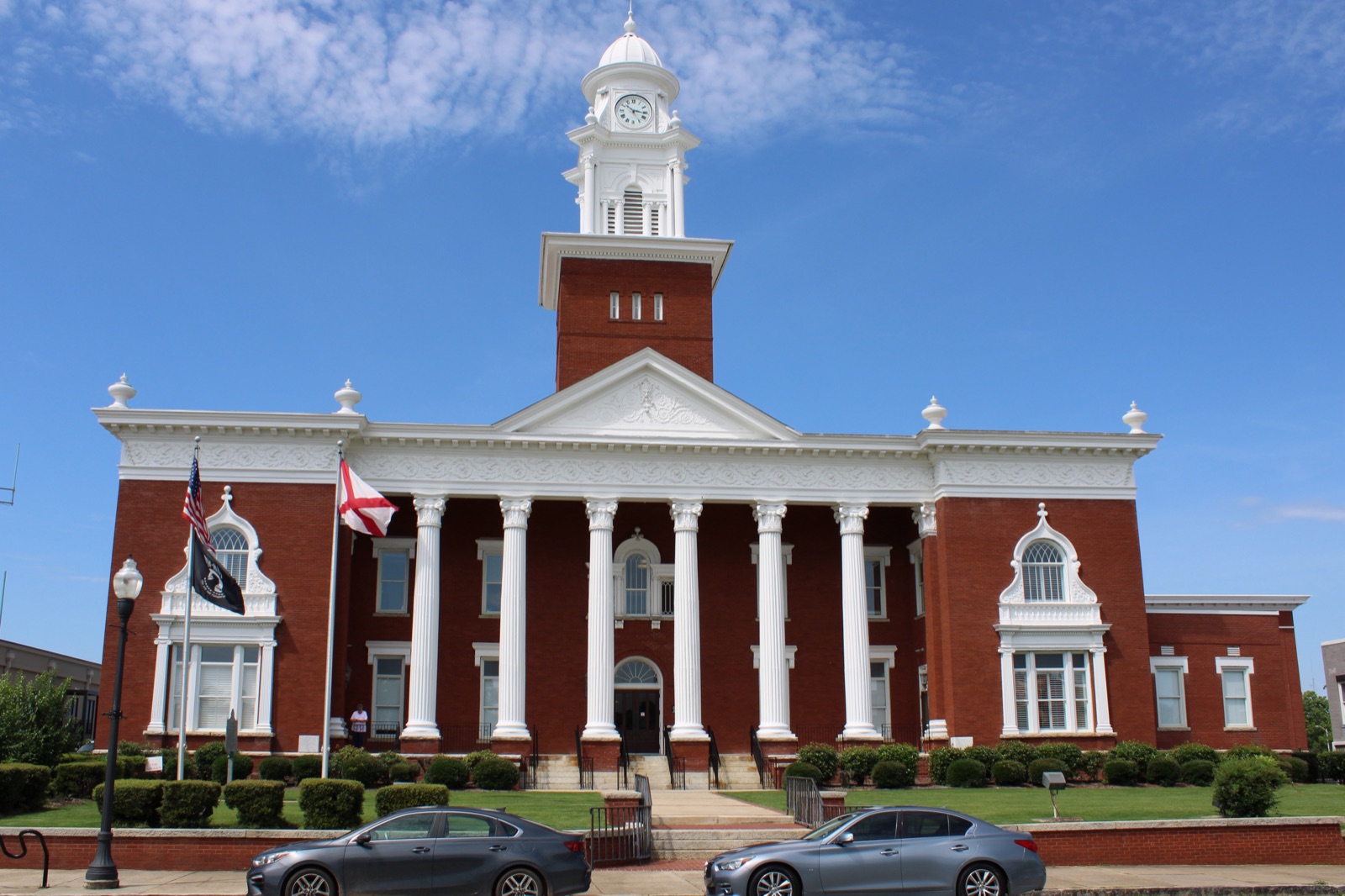 A Southern county courthouse of brick and white columns standing at the center of a town square, ringed by storefronts and old shade trees.
