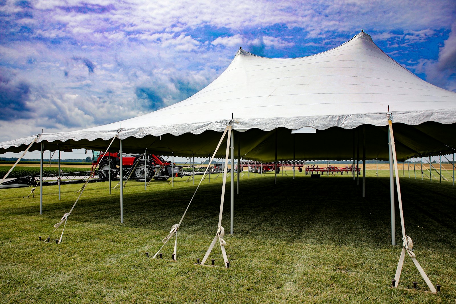 A revival tent lit from within at dusk, folding chairs and a piano set out on the grass as people gather.