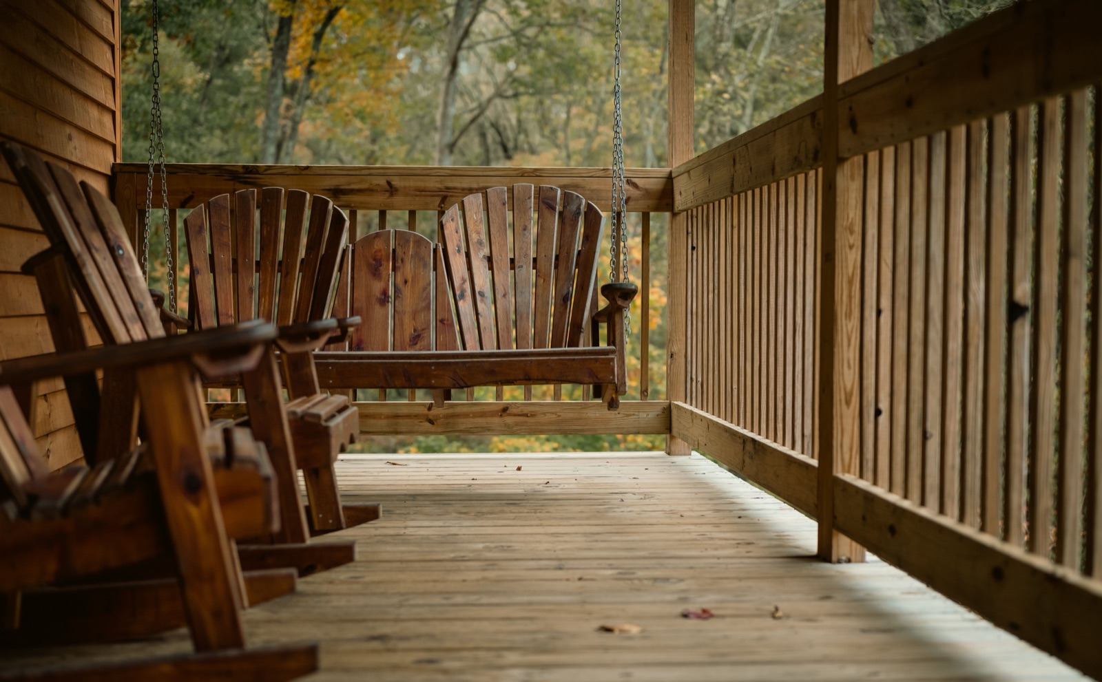A deep Southern front porch at dusk with rocking chairs, a porch swing, and a screen door, the yard going gold in the last light.