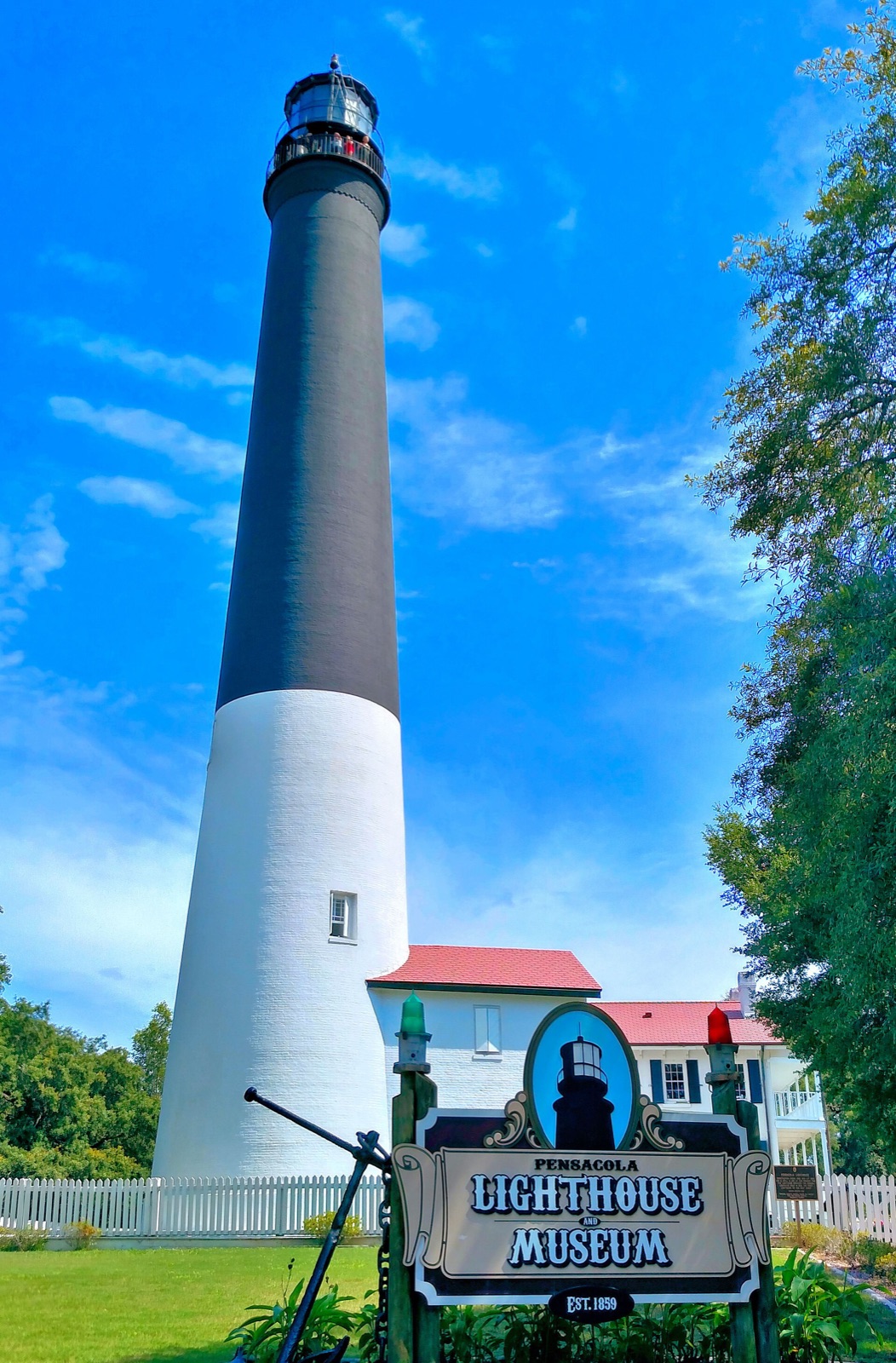 The white Pensacola Lighthouse with its black upper half rising above the pines of the Florida panhandle coast.