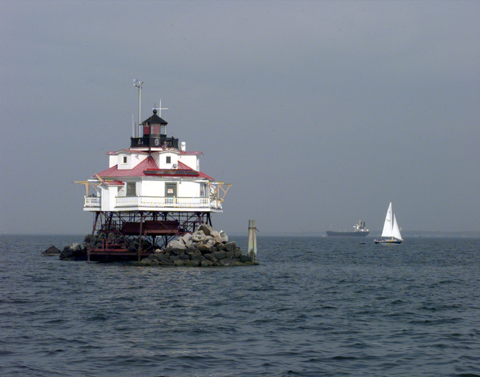 A screw-pile lighthouse, a small cottage raised on iron legs, standing alone over the shallow water of a sound.