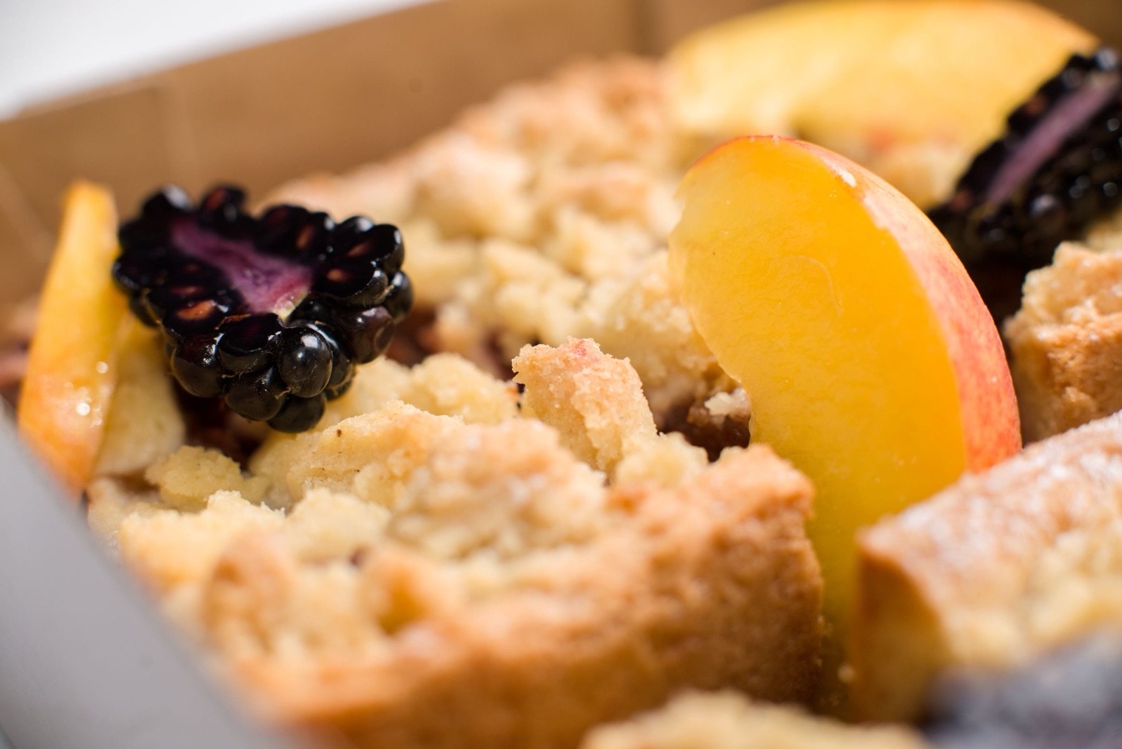 A golden peach cobbler with a crumbly crust, peach slices, and blackberries in a baking dish.