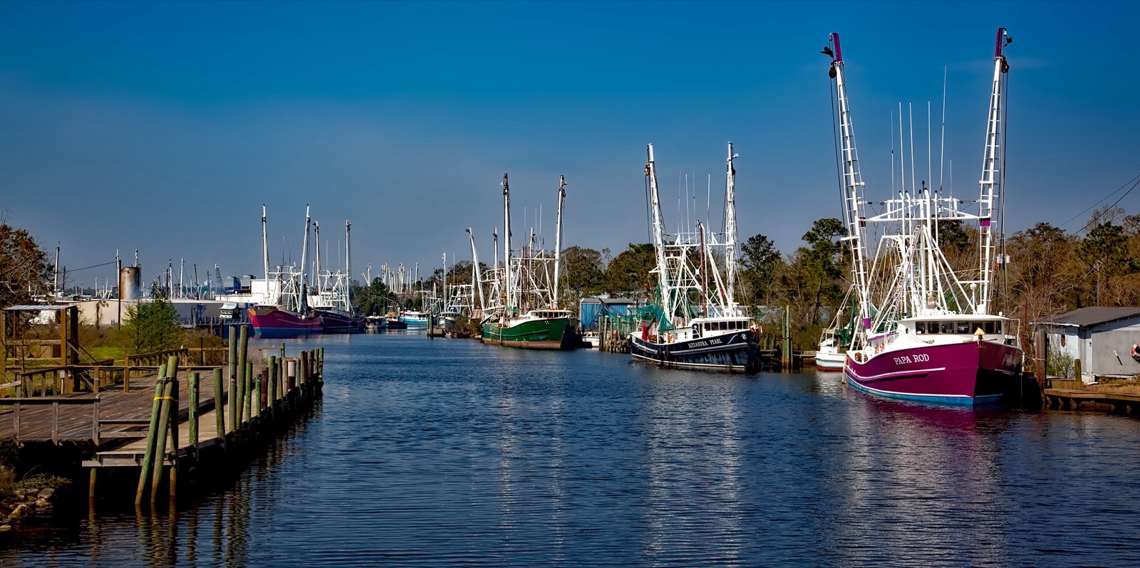 Colorful shrimp boats with tall outriggers docked along a canal at Bayou La Batre, Alabama.