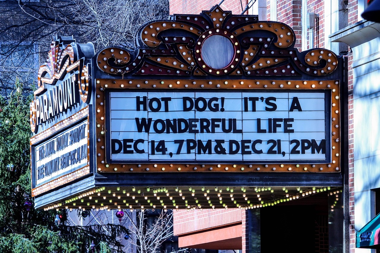 A lit vintage theater marquee glowing over a small-town sidewalk at dusk.