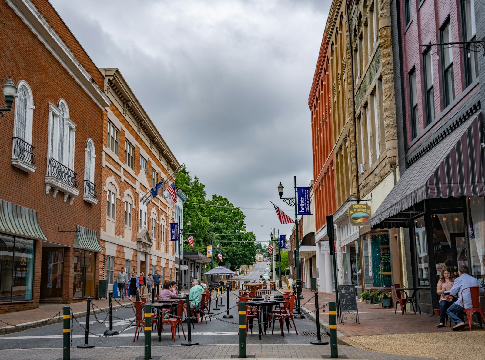 A downtown street in Staunton, Virginia, lined with Victorian brick storefronts and sidewalk cafe tables under an overcast sky.