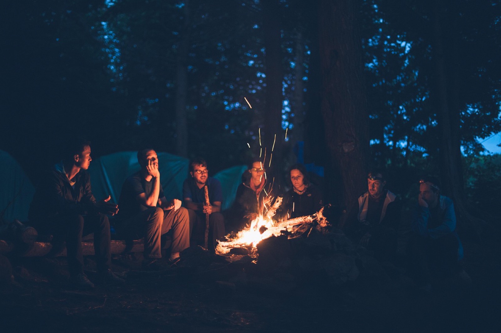 People gathered in a circle around a blazing bonfire at night.
