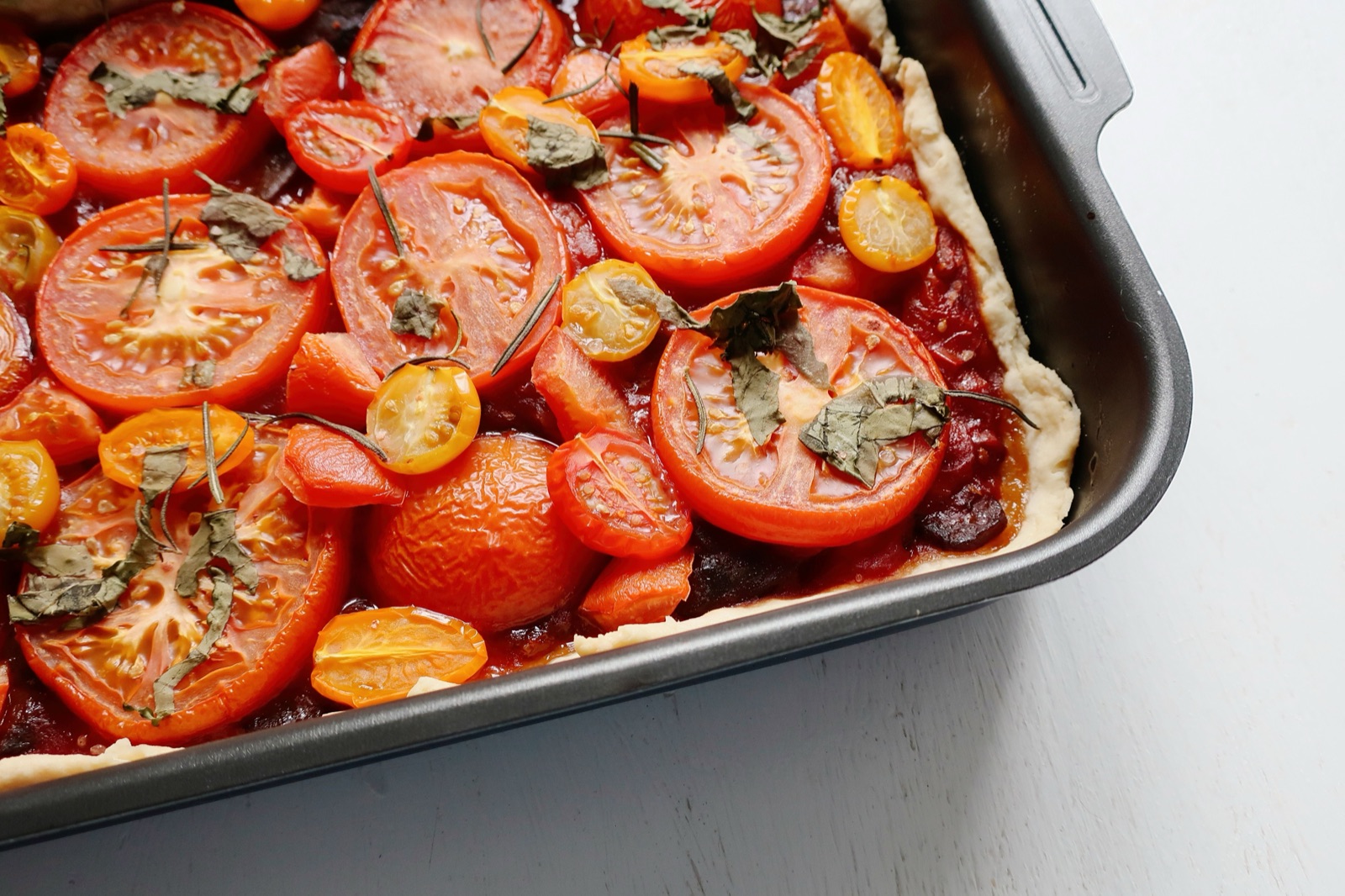 A baked tomato pie topped with fresh herbs in a baking dish.