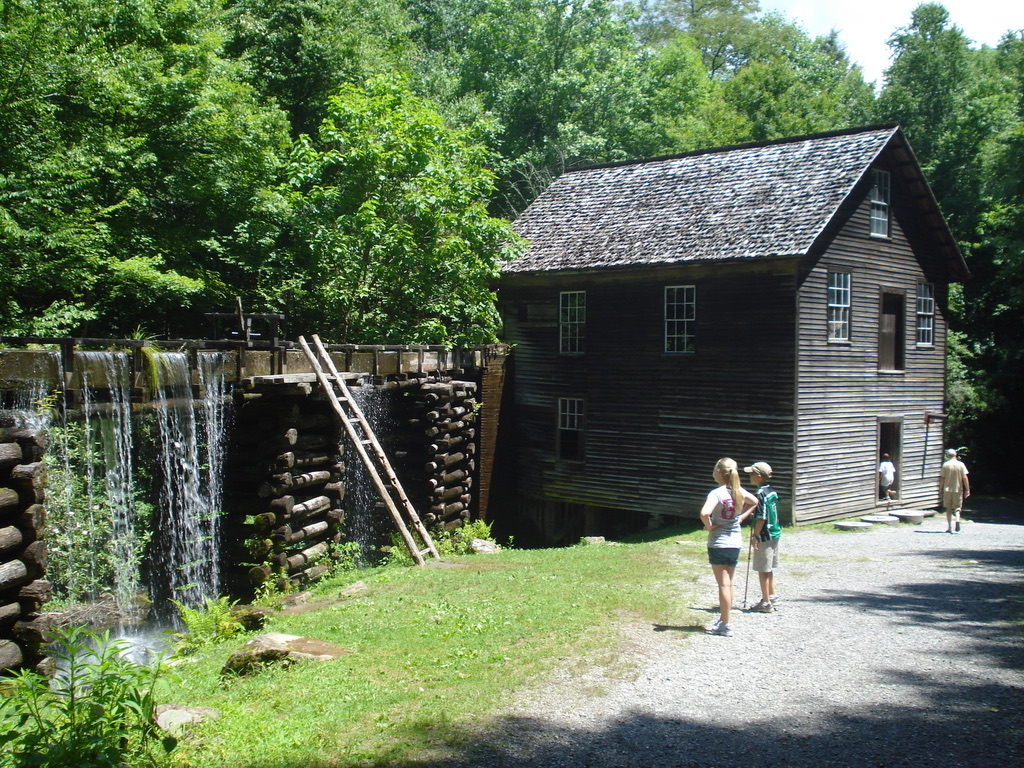 Water spilling down the wooden flume beside a tall weathered grist mill in the woods.